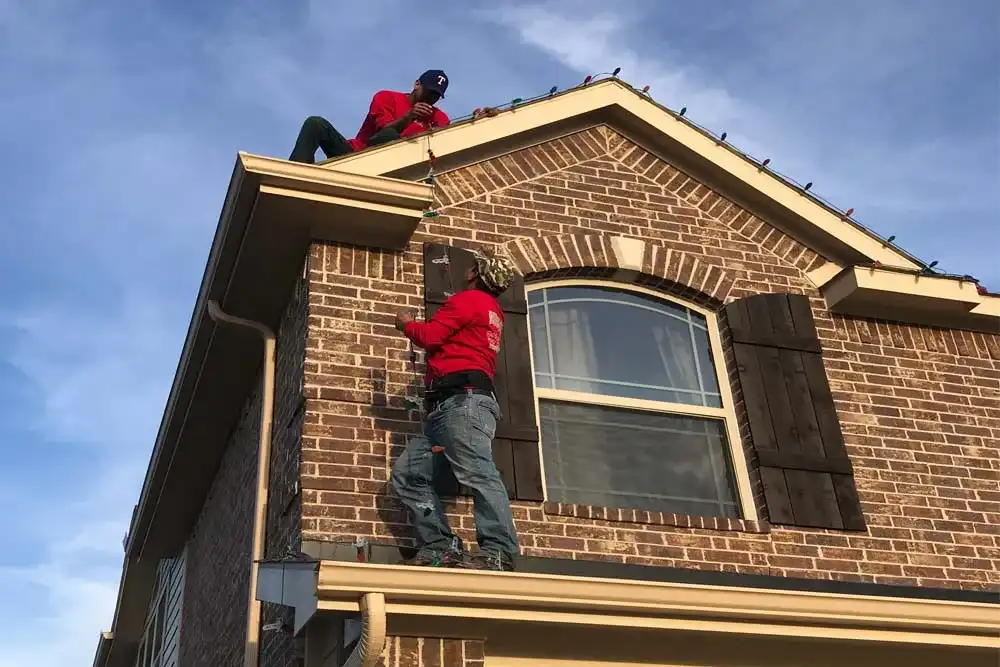 Installers on a ladder and roof hanging Christmas lights on a brick home