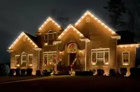 Brick home with warm white lights on every gable and wreaths in the windows