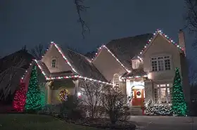 Home with multicolor lights on the gables and evergreens wrapped in green and red lights