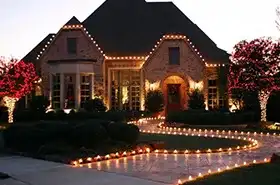 Home with a lit walkway and trees wrapped in red lights at dusk