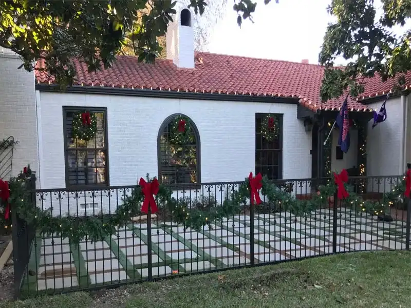 Garland with red bows on a front fence and wreaths on the windows of a white home