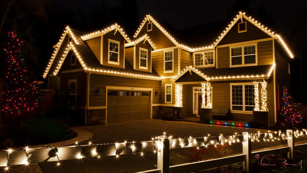 Two-story home with every gable outlined in warm white Christmas lights at night
