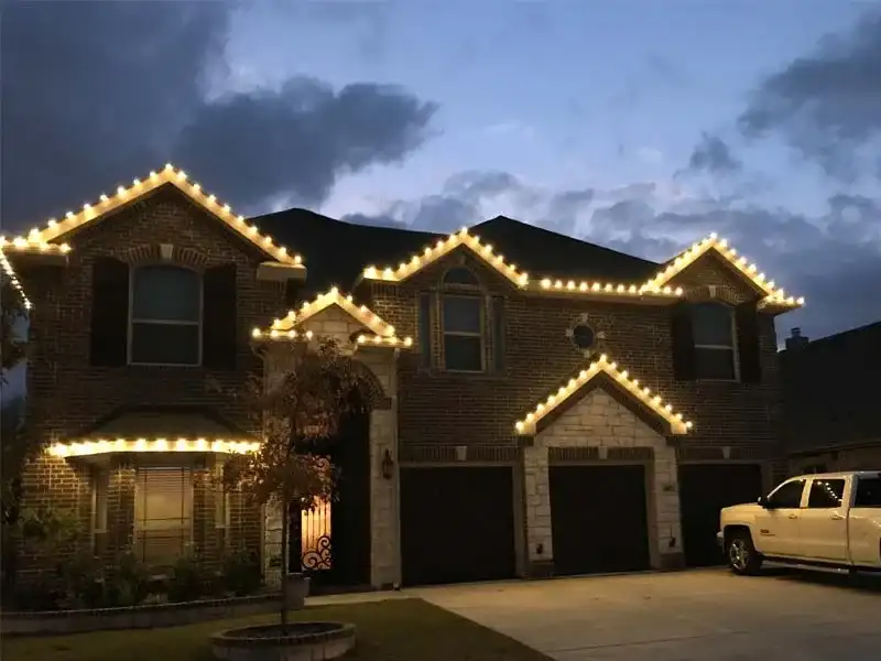 Two-story home with warm white Christmas lights along the roofline at dusk